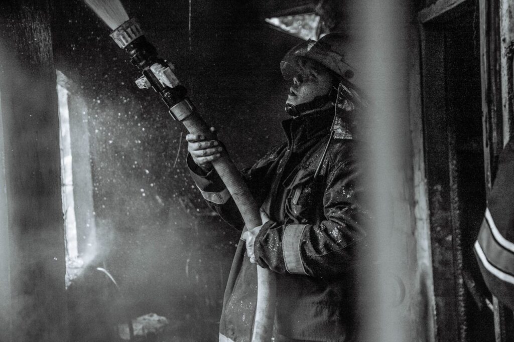 A determined firefighter battles smoke and flames with a hose in this monochrome scene.