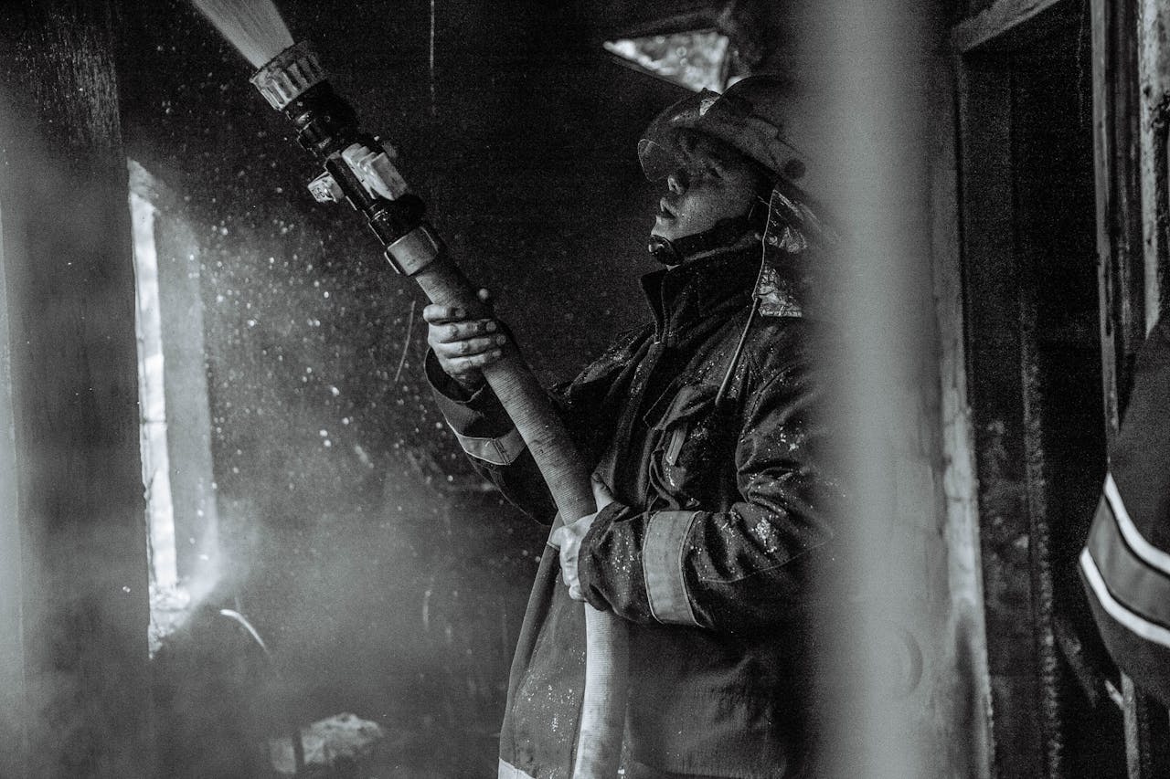 A determined firefighter battles smoke and flames with a hose in this monochrome scene.