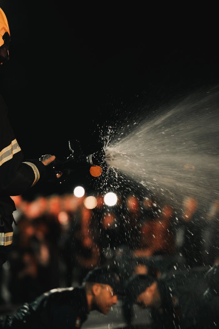 A firefighter uses a hose to spray water at night, capturing dramatic motion and lighting.